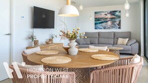 A modern living room with a round wooden dining table, grey sofa, and a large painting of a seascape. - The Palm Escape – Seaview, Pool & Terrace | Higueron West, Fuengirola (Fuengirola)