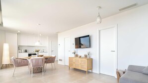 A modern living room with a grey sofa, a wooden coffee table, and a dining area with wicker chairs. - The Palm Escape – Seaview, Pool & Terrace | Higueron West, Fuengirola (Fuengirola)