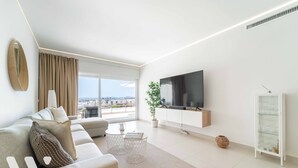 A modern living room with a sofa, TV, and a view of the city. - The Sunset Vista – West-Facing Mountain & Valley Views with Pool | Carvajal, Fuengirola (Benalmádena)