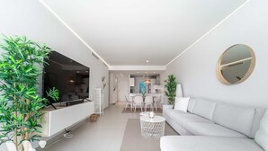 A modern living room with a sofa, a dining area, and a kitchen in the background. - The Sunset Vista – West-Facing Mountain & Valley Views with Pool | Carvajal, Fuengirola (Benalmádena)