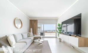 Ein modernes Wohnzimmer mit Sofa, Couchtisch, Fernseher und einem großen Fenster mit Blick.