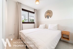 Ein modernes Schlafzimmer mit zwei Betten, einem Vorhangfenster, einem Wandventilator und einem Nachttisch.