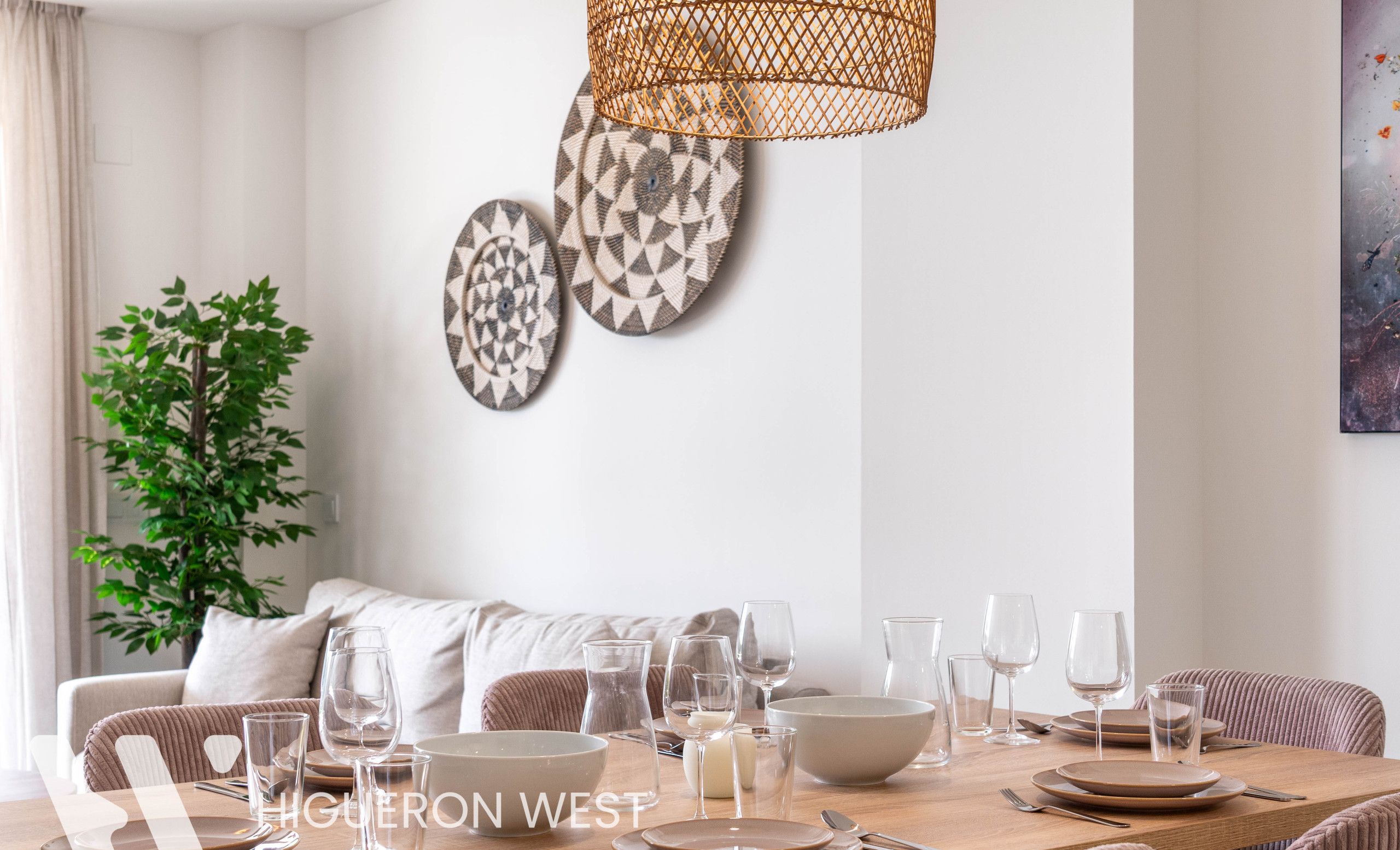 A dining area with a wooden table set for six, surrounded by cushioned chairs. There are decorative plates on the wall and a plant in the corner.