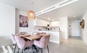 Cocina moderna con armarios blancos, una isla de madera y un comedor con sillas tapizadas en rosa.