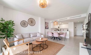 Una sala de estar moderna con un sofá, una mesa de centro y un comedor con sillas. Se observa una cocina al fondo.