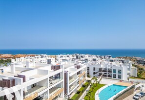Un moderno complejo residencial con varios edificios blancos, una piscina y vistas al mar.