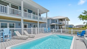 A pool area with a rectangular pool, white deck, and blue Adirondack chairs. - 5513 E Pelican Drive 5 bedrooms, private pool, and easy beach access. (Oak Island)