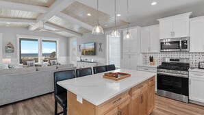 A modern kitchen with white cabinets, stainless steel appliances, and a large island. - 5513 E Pelican Drive 5 bedrooms, private pool, and easy beach access. (Oak Island)