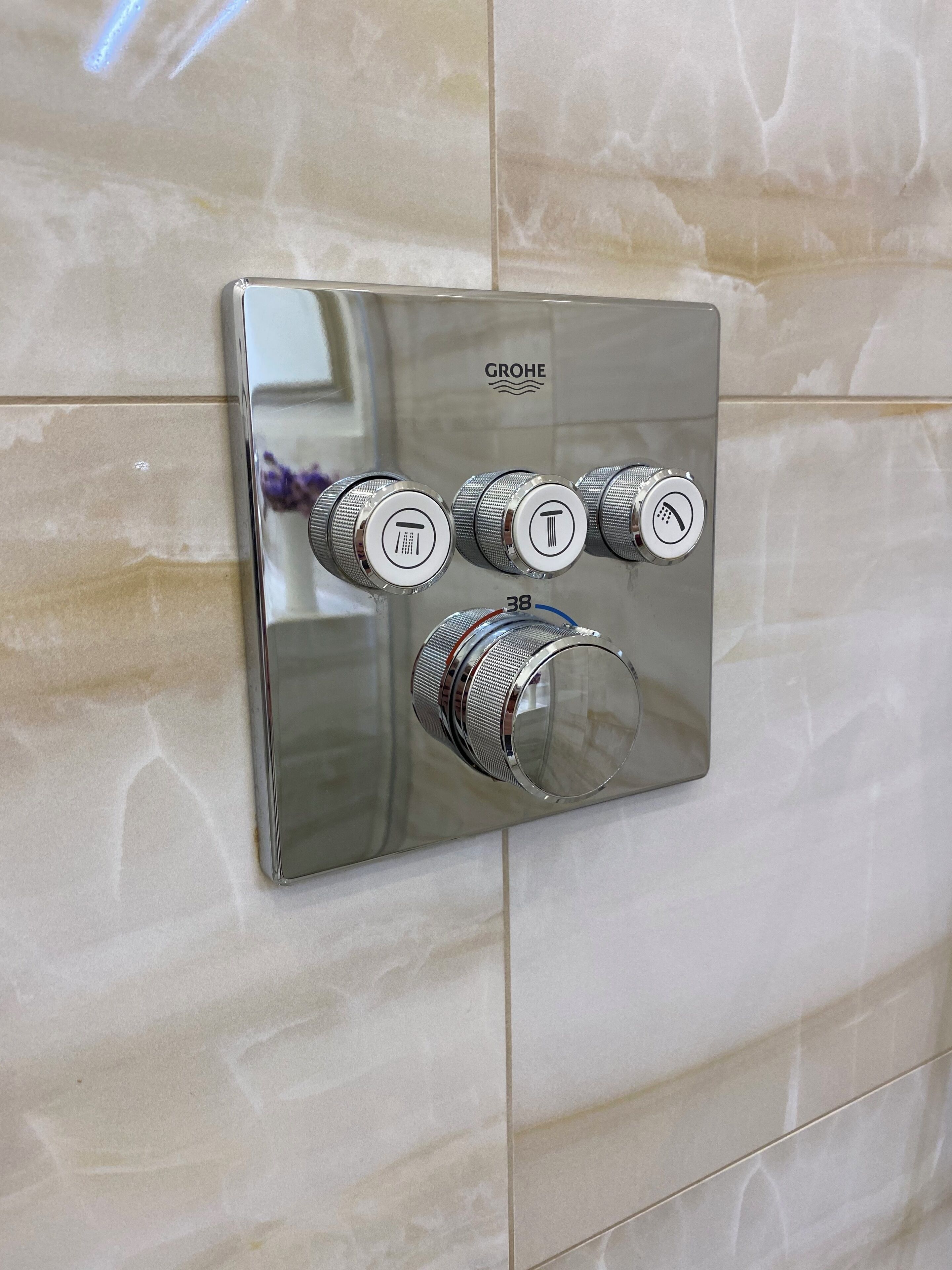 A GROHE bathroom control panel with three knobs and a single lever, mounted on a tiled wall.