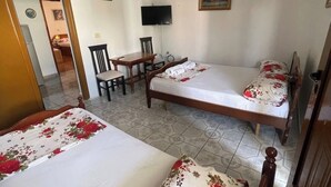 A hotel room with two single beds, a desk, a chair, a television, and a door leading to another room. - Olympia’s Apartment – Spacious Retreat for Up to 6 Guests (Fishta)
