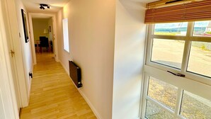 A hallway with wooden flooring, white walls, a radiator, and a window with a view of the outdoors. - Dolphin Bay - Beautiful 1 Bedroom Apartment (Ardersier)