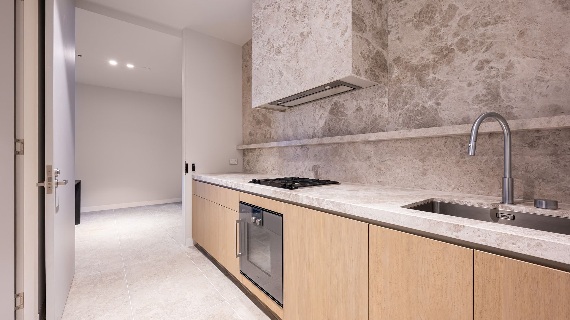 A modern kitchen with a built-in dishwasher, a stainless steel sink, and a marble backsplash.