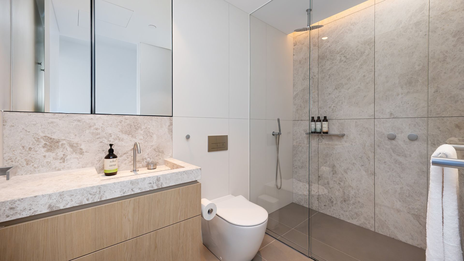 Ein modernes Badezimmer mit Marmorwaschtisch, Toilette, Duschkabine und Handtuchhalter.