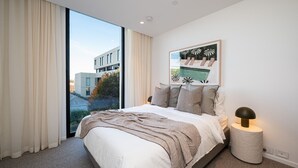A modern bedroom with a large bed, a view of a building through a window, and a framed artwork on the wall. - Signature 81 in Brighton (Brighton)