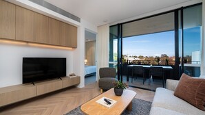 A modern living room with a flat-screen TV, a sofa, a coffee table, and a dining area with chairs. - Signature 81 in Brighton (Brighton)