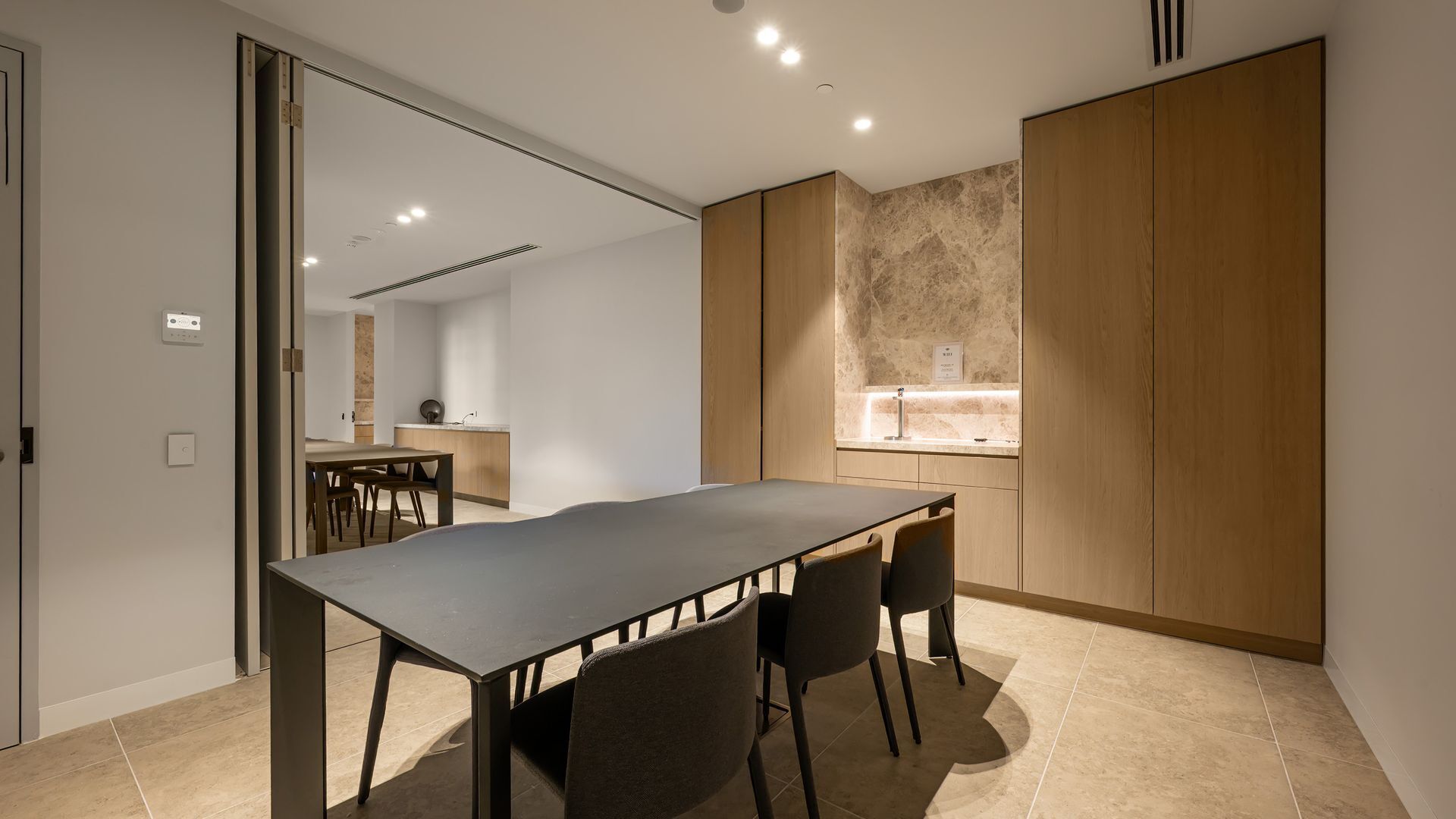 A modern kitchen with a large island, a dining area with a long table and chairs, and a wooden wardrobe.