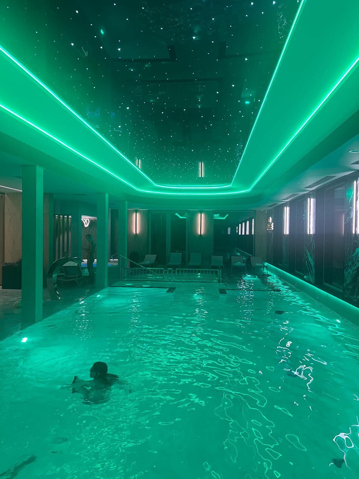 A swimming pool with a starry ceiling and green ambient lighting.