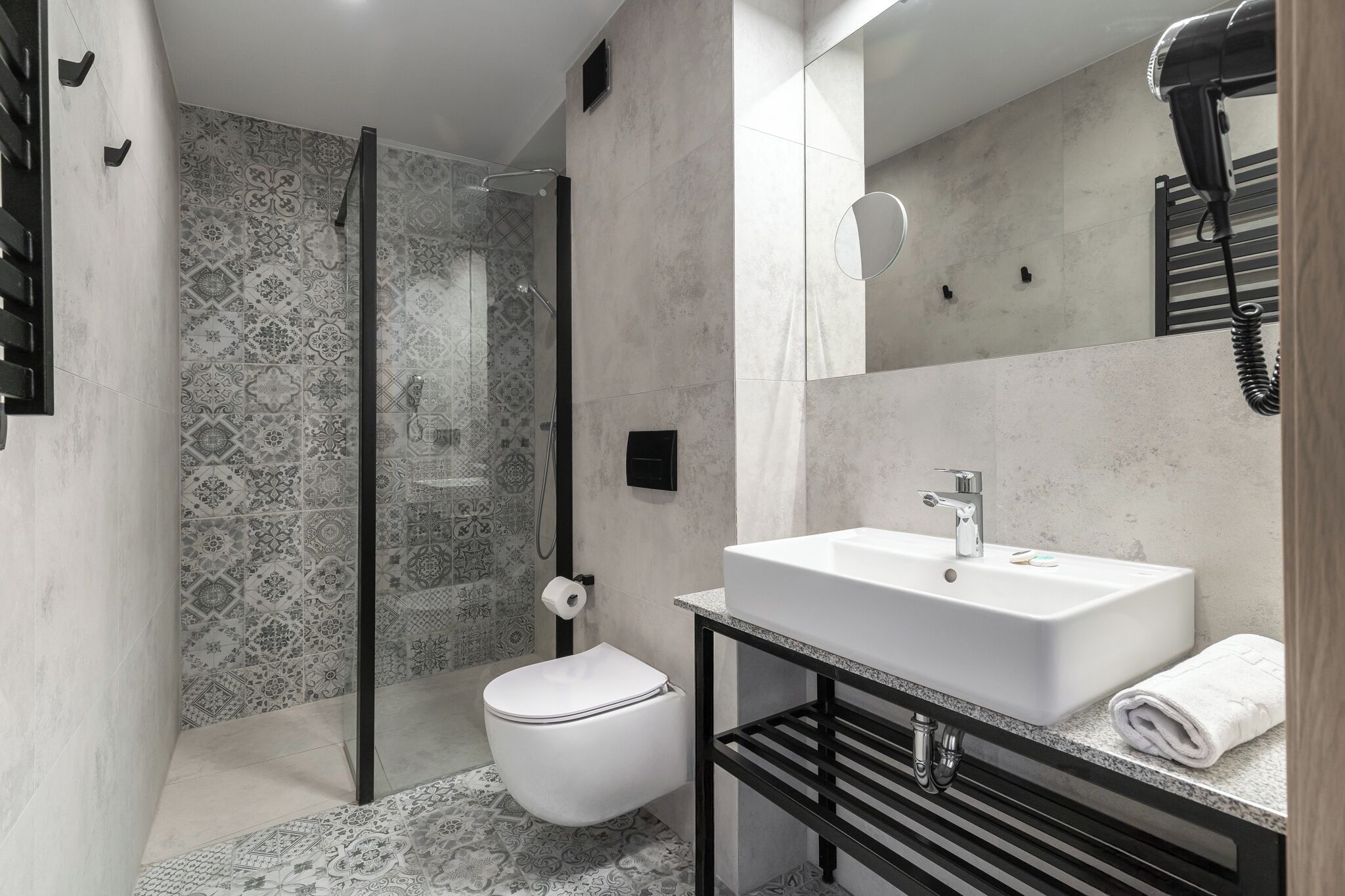 A modern bathroom with a walk-in shower, a toilet, a sink with a towel, and a hairdryer.