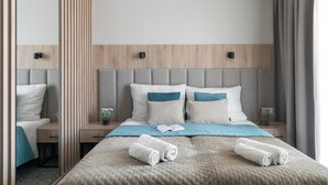 A neatly made bed with a grey headboard, two pillows, and two rolled towels. - Rezydencja Ambre (Łeba)