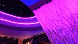 A modern indoor pool area with a waterfall feature, a neon sign, and a marble wall. - Rezydencja Ambre (Łeba)