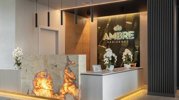 A reception desk with a large illuminated artwork, a sign for 'AMBRE RESIDENCE', and two potted white orchids.