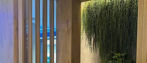 Una persona sentada en un banco acolchado con vistas a una piscina y una pared verde con plantas colgantes.