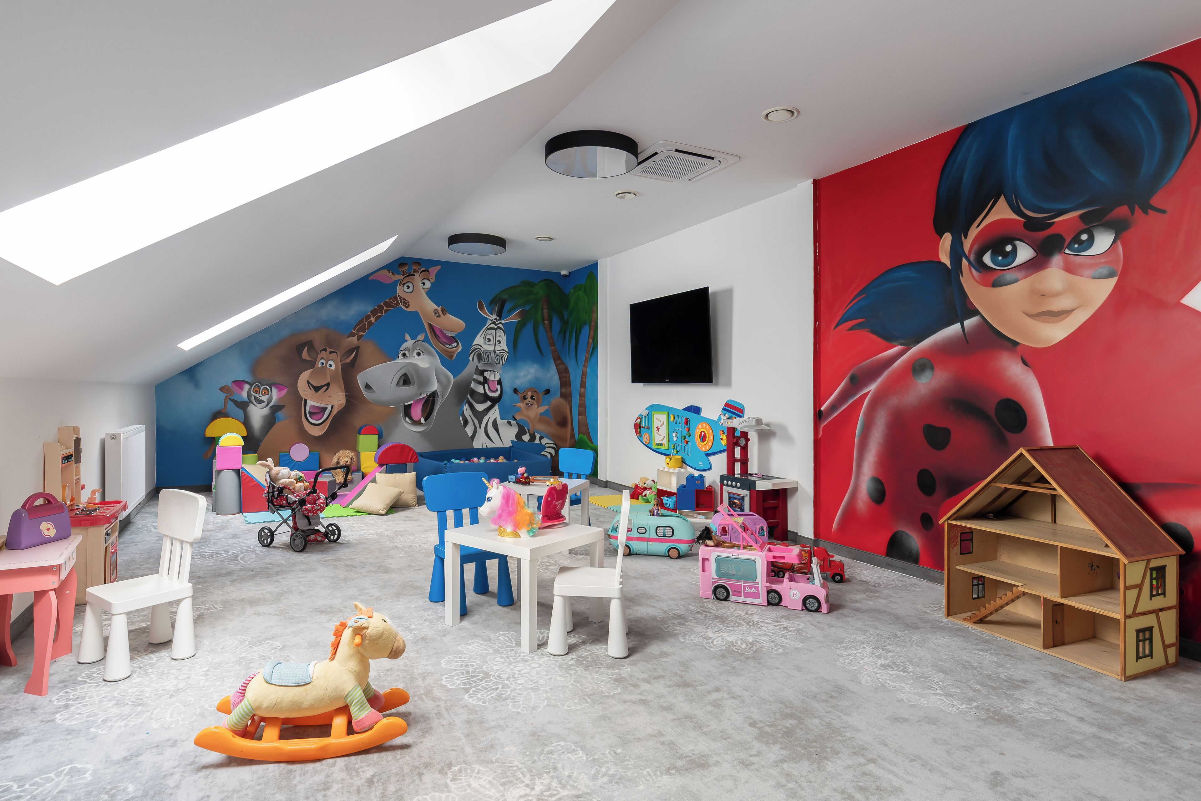 A child's playroom with a sloped ceiling, a mural, and various toys.