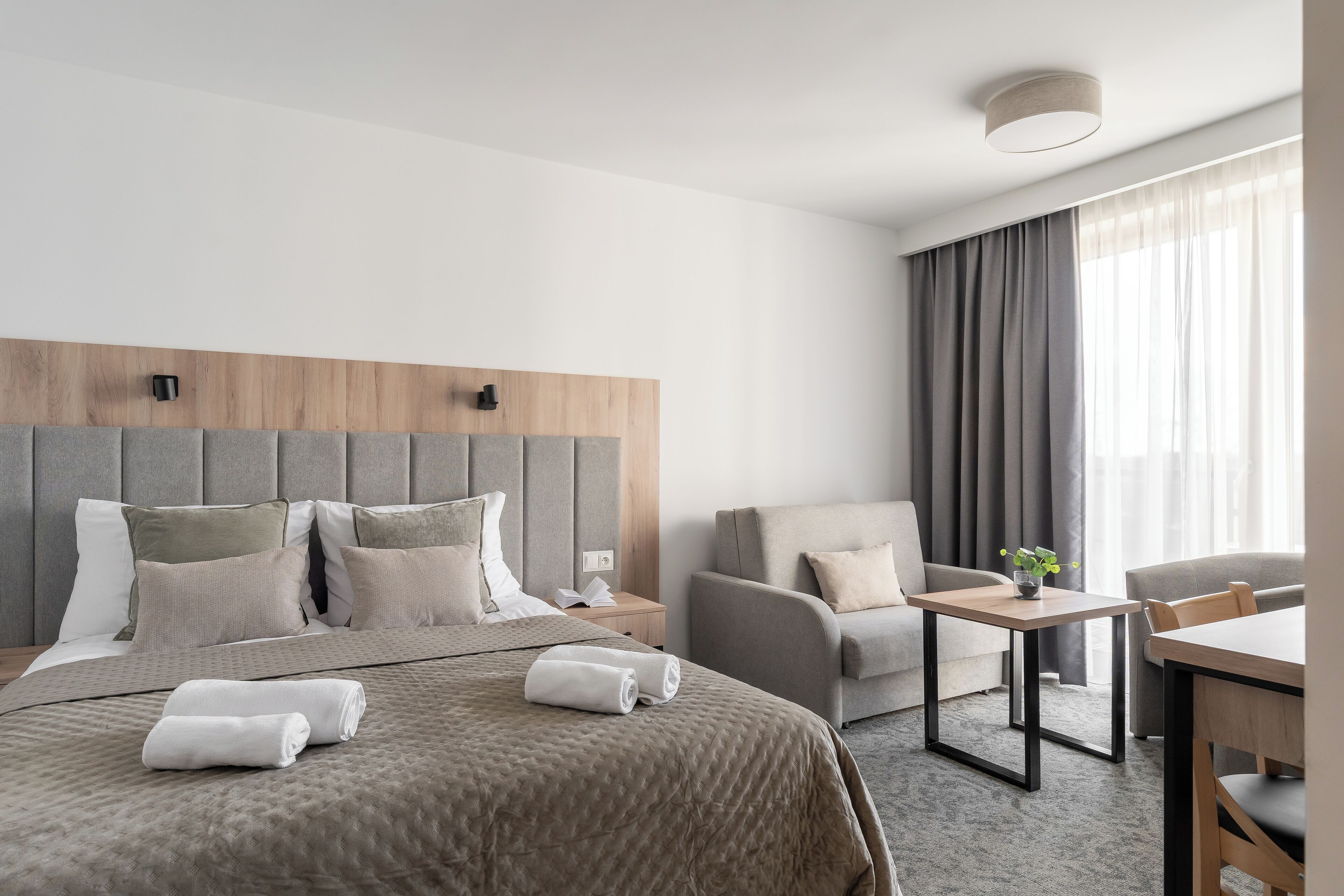 A modern hotel room with a large bed, a sofa, a small table, and a desk.