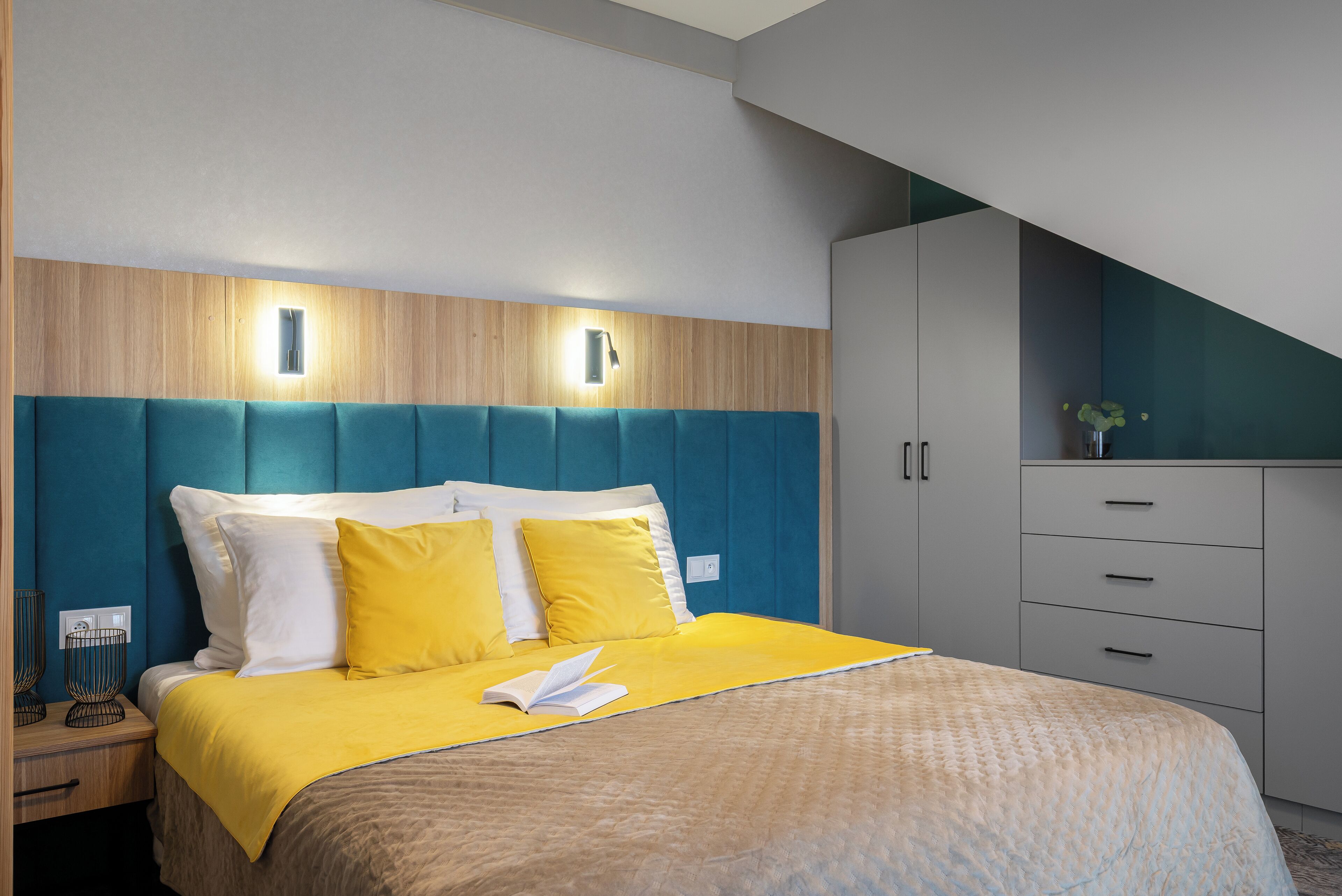 A modern hotel room with a bed, bedside tables, a nightstand, and a built-in wardrobe.