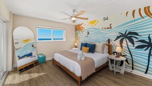 A bedroom with a bed, a ceiling fan, a small table with a lamp, a window, and a wall mural. - Luxury Condo-Gulf Front-Fully Loaded For Families (Panama City Beach)