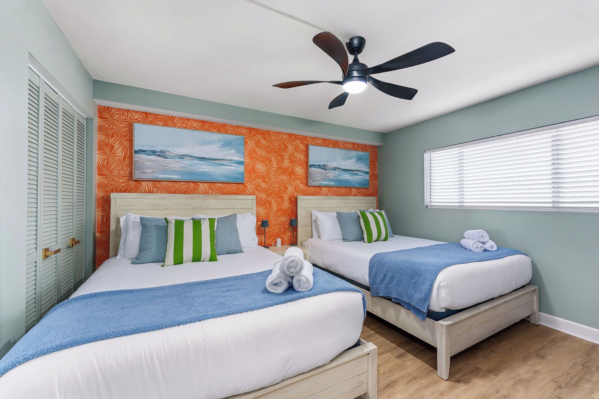 A hotel room with two beds, a ceiling fan, and artwork on the walls.