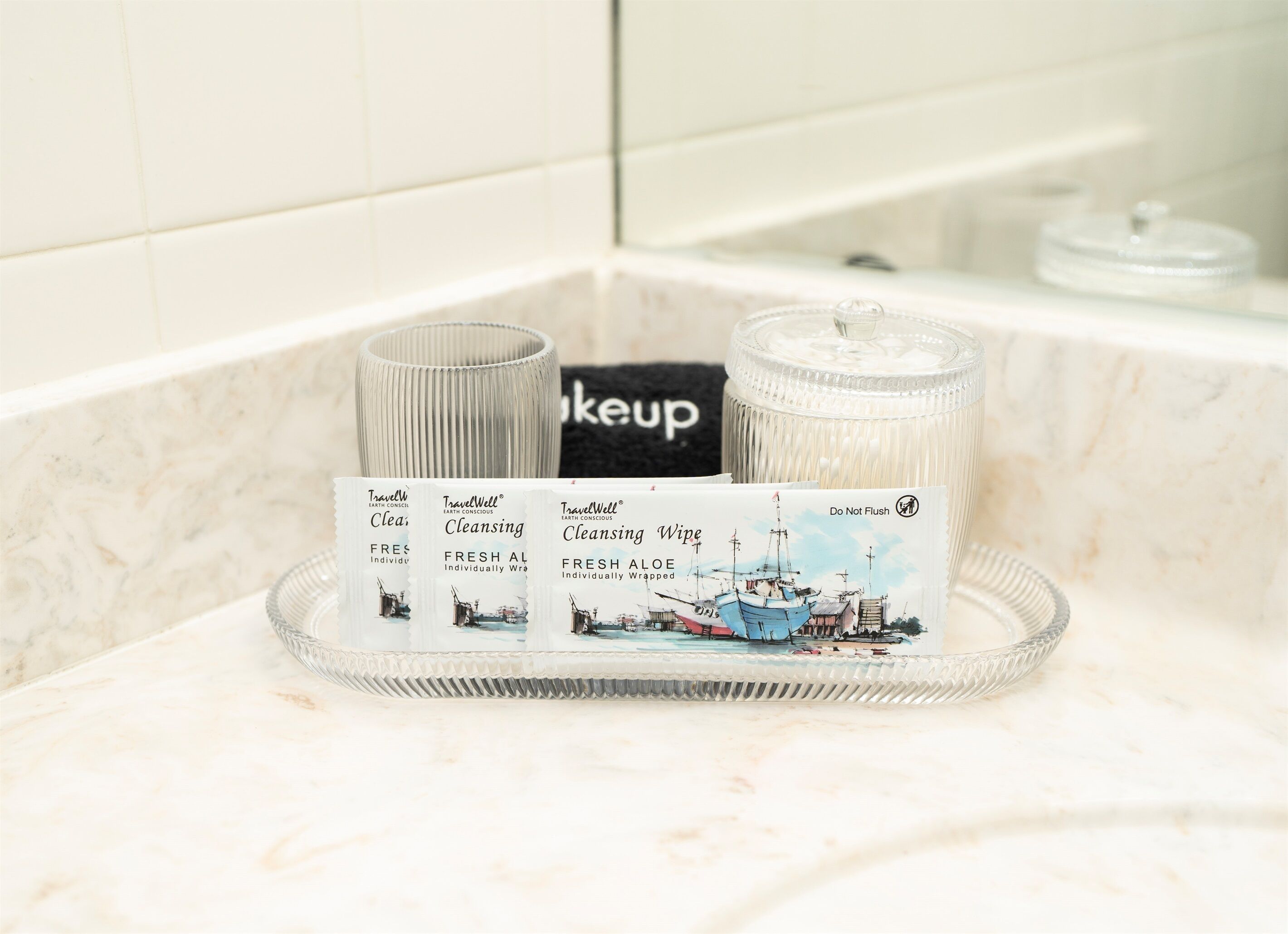 Un meuble-lavabo de salle de bain doté d’un plan de toilette en marbre, d’un porte-savon en verre et de trois produits nettoyants de la gamme TravelWell.