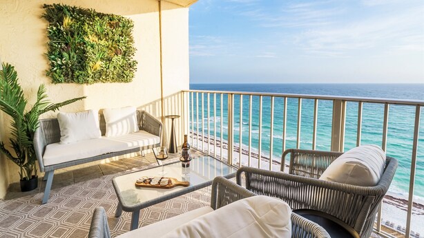A balcony with a sofa, wicker chairs, a glass table, and a potted plant. - Luxury Condo-Gulf Front-Fully Loaded For Families (Panama City Beach)
