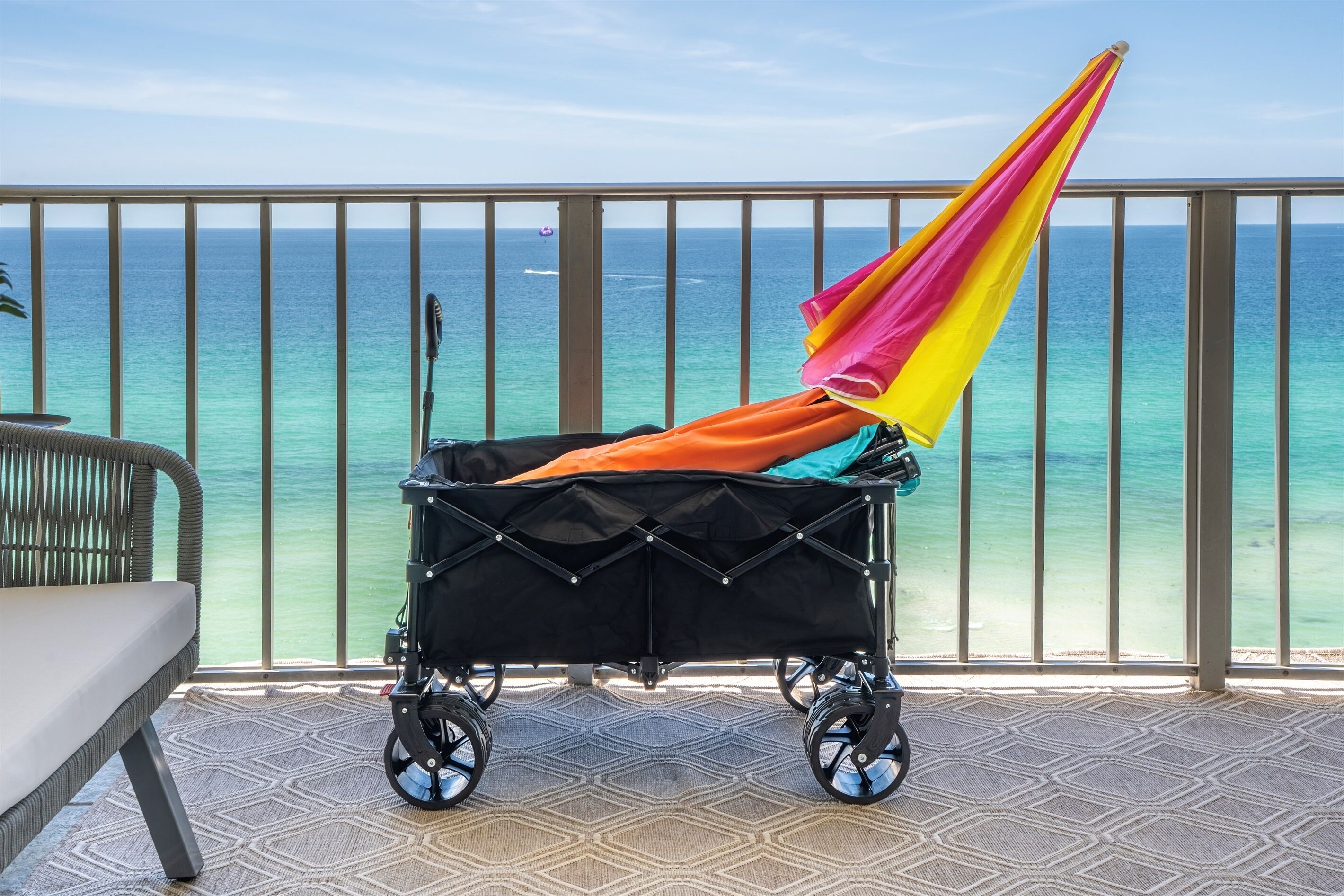 Carrinho de bebê com toldo colorido numa varanda com vista para o mar.