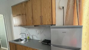 A kitchen with wooden cabinets, a stainless steel sink, and a DeLUX refrigerator. - Olympia Triple Room – Cozy & Central Stay for 3 Guests (Fishta)