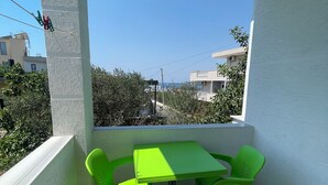 A balcony with a green table and chairs, a small stool, and a view of buildings and trees. - Olympia Triple Room – Cozy & Central Stay for 3 Guests (Fishta)
