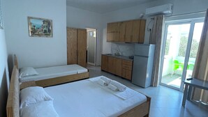 A modern hotel room with two wooden beds, a kitchenette, and a balcony with a green chair. - Olympia Triple Room – Cozy & Central Stay for 3 Guests (Fishta)