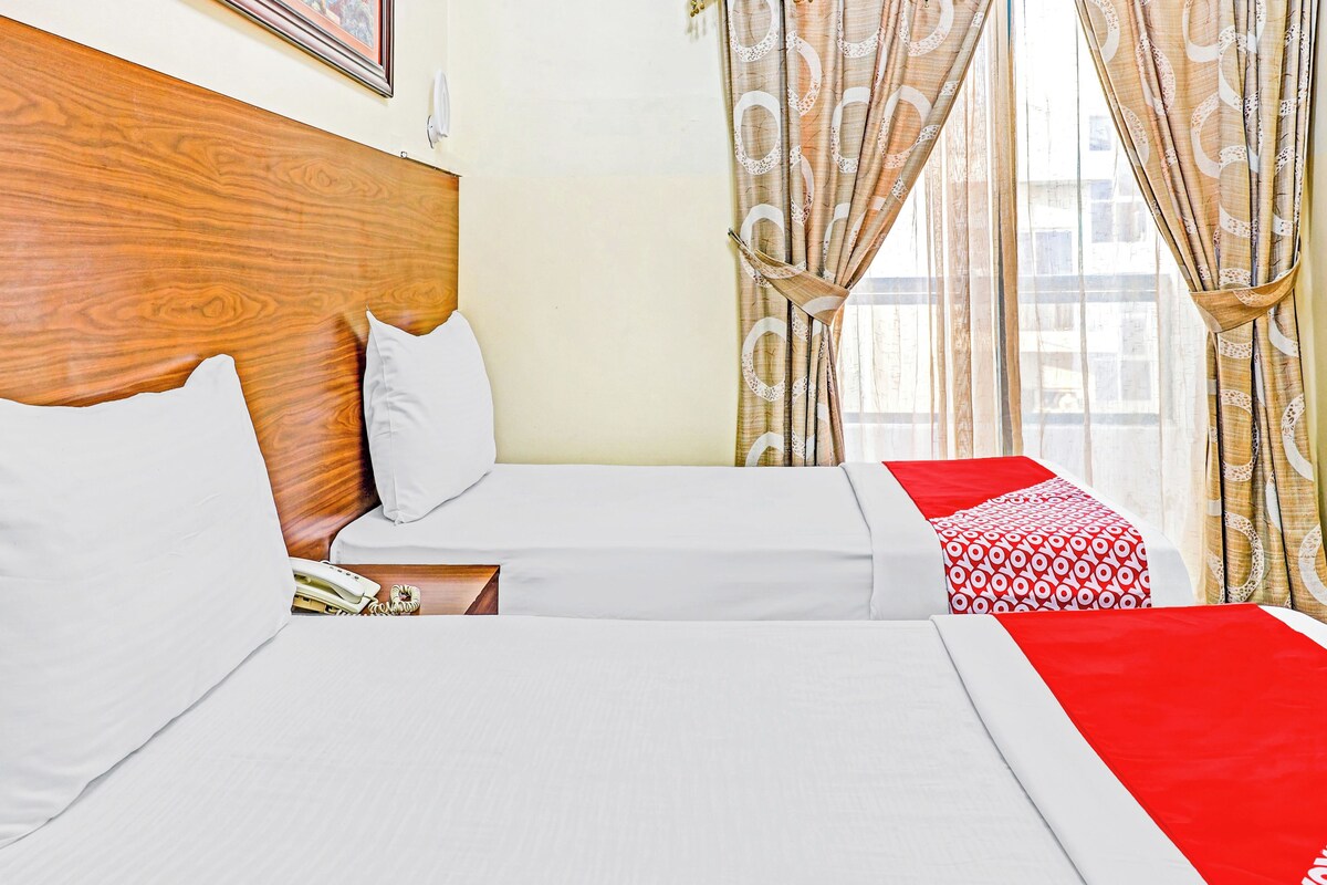 Habitación de hotel con dos camas, cabecera de madera, ropa de cama blanca y una manta estampada en rojo y blanco.