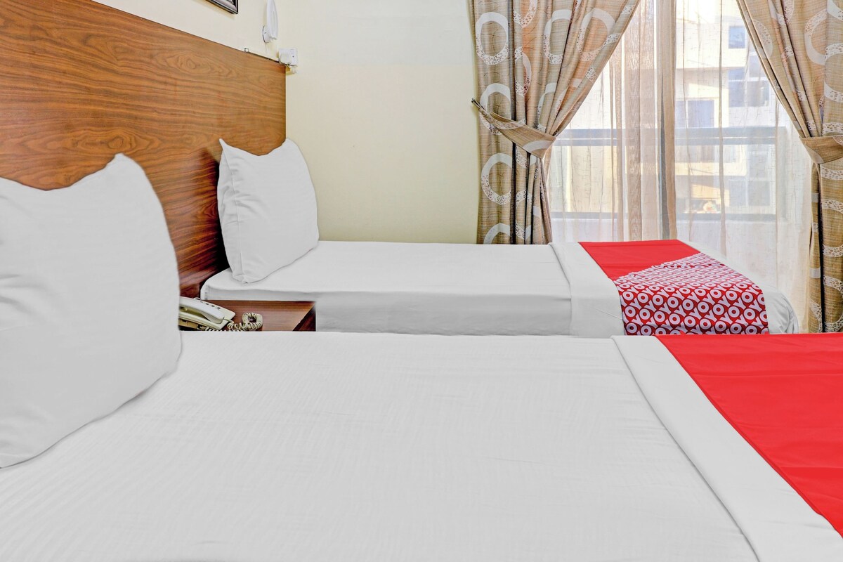 Habitación de hotel con dos camas, cabecera de madera, teléfono y cortinas estampadas.