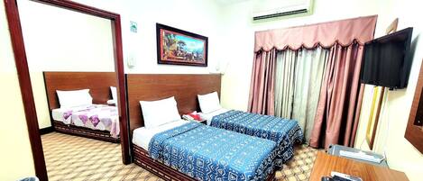 A hotel room with two beds, a wooden headboard, a painting on the wall, a TV, and a desk with a remote control.