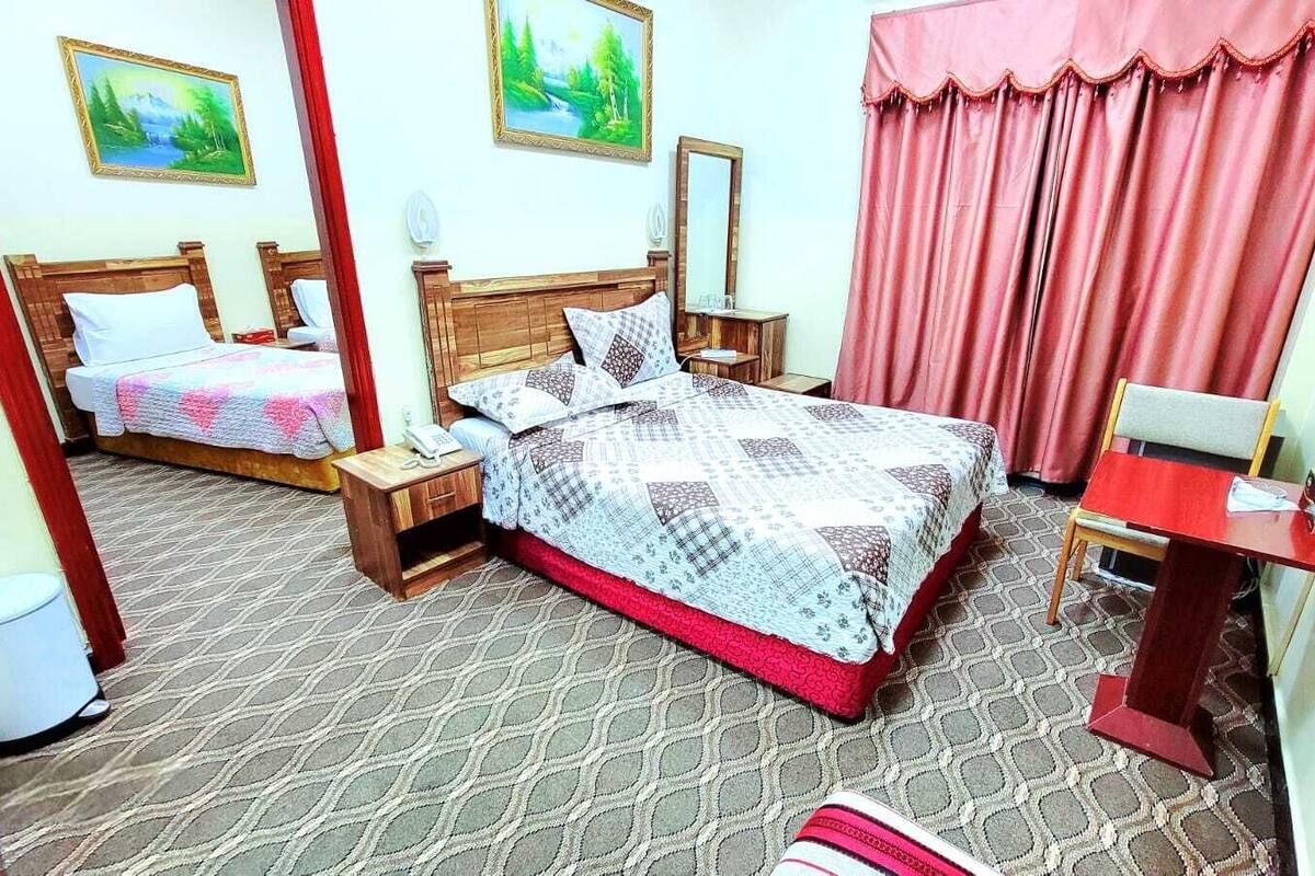 A hotel room with two beds, a small table, a chair, a mirror, and a red curtain.