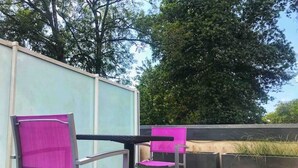 En terrasse med to stole og et bord, omgivet af en lav mur og et stort træ.