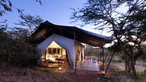 A tented accommodation with a bed, seating area, and a view of the surrounding landscape. - Basecamp Wilderness (Maasai Mara)