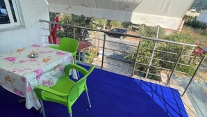 A balcony with a table and chairs, a blue mat, and a view of the surrounding area. - Olympia Double Room with Garden View – Cozy & Peaceful Stay! (Fishta)