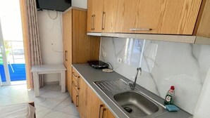 A compact kitchen with wooden cabinets, a stainless steel sink, and a small table. - Olympia Double Room with Garden View – Cozy & Peaceful Stay! (Fishta)