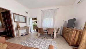 A cozy living room with a sofa, a coffee table, and a TV. There is a dining area with a table and chairs, and a kitchen area with a wooden cabinet and a TV. - Rakos ter 30 (Budapest)