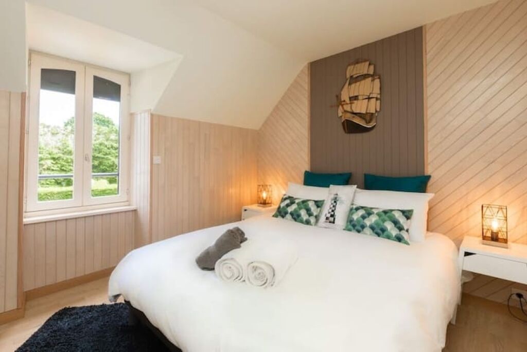 A bedroom with a large bed, a window, and a wall-mounted light fixture.