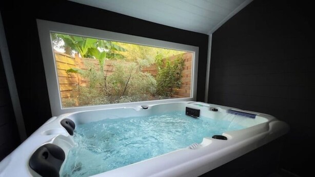 A hot tub with a window view of a garden. - 🏖 5 min from Bénodet and the ocean - comfortable rooms with SPA included 🌿 (Pleuven)