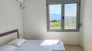 Ein Schlafzimmer mit Bett, einem Fenster mit Blick auf Grünflächen und Hügel sowie einer Klimaanlage an der Wand.