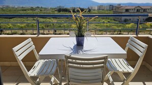 Ein Balkon mit Tisch und Stühlen, einem Blumentopf und Blick auf entfernte Gebäude und Berge.